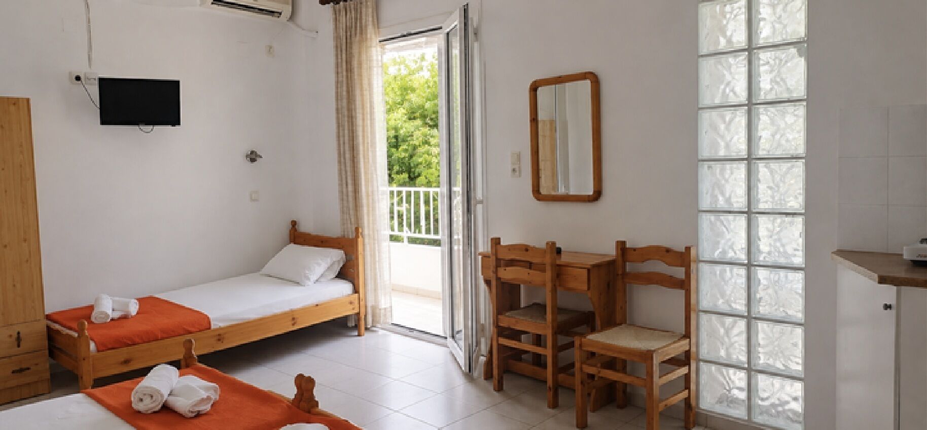 Ein Zimmer mit zwei Holzbett, einem Holzstuhl, einem Spiegel und einem Fenster mit Milchglas.