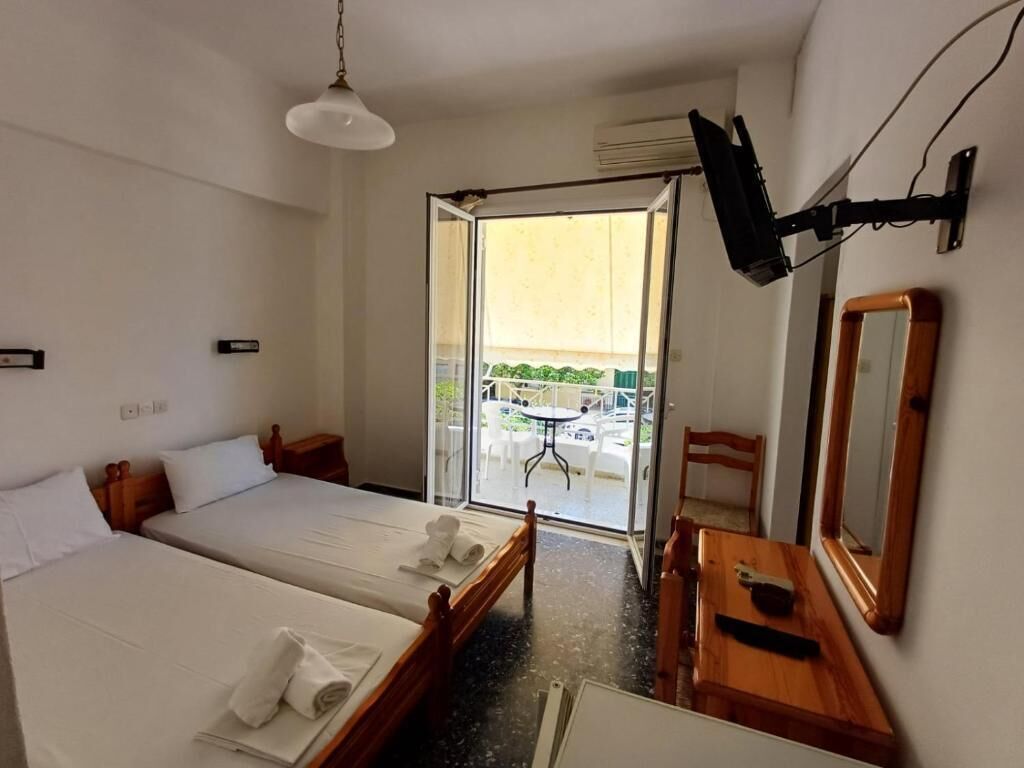 Habitación de hotel con dos camas, un aparador de madera, un espejo y un balcón con mesa y sillas.