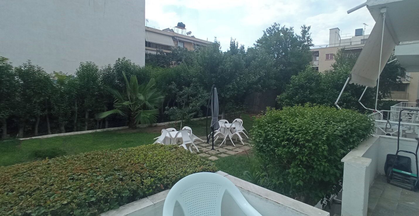 Un patio con césped, sillas de plástico blanco y una fuente de agua.