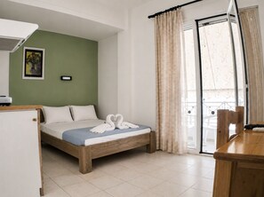 A hotel room with a bed, a desk, a chair, a window with curtains, and a wall-mounted air conditioner.
