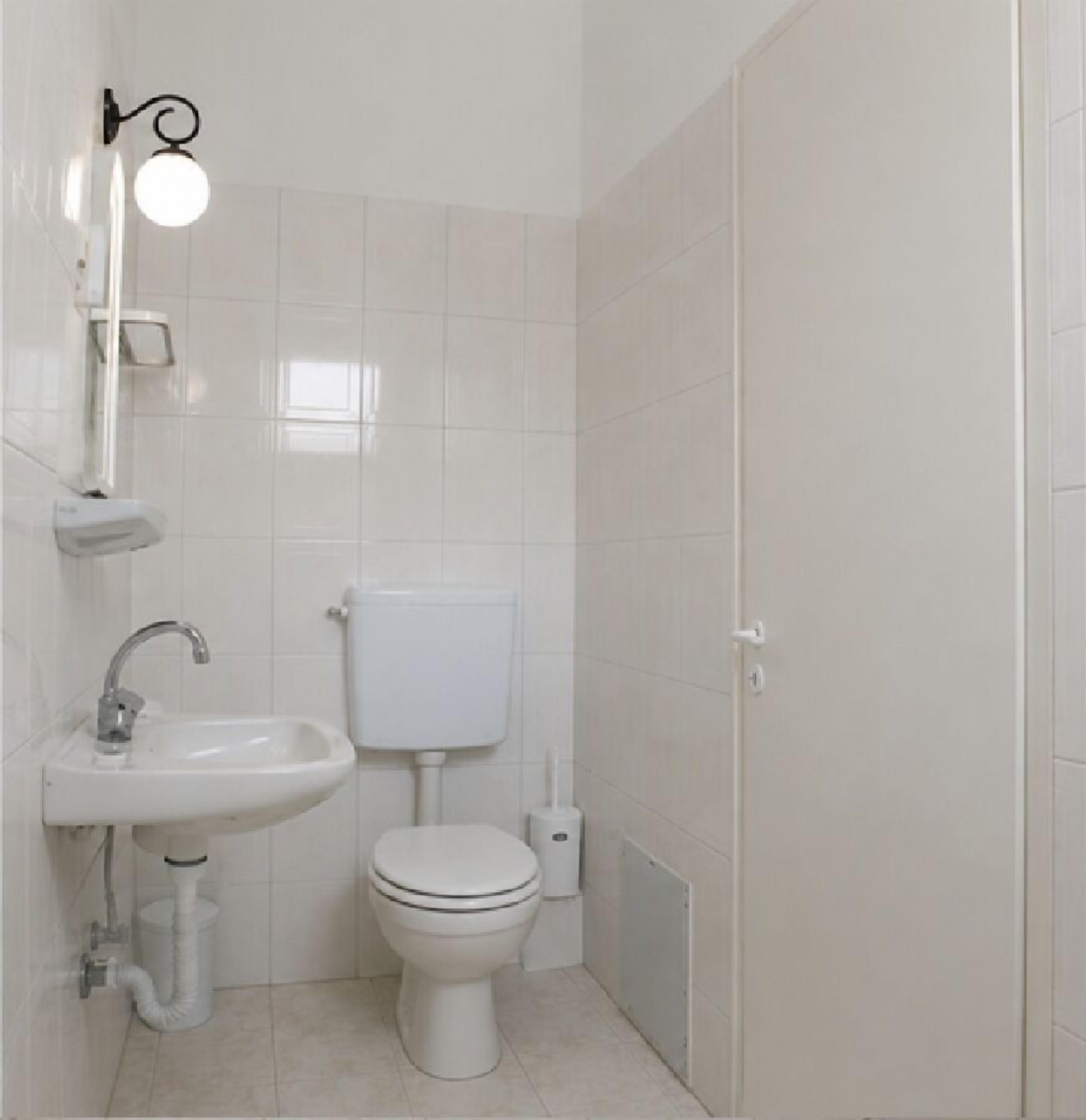 Un baño con inodoro, lavamanos y una lámpara en la pared.