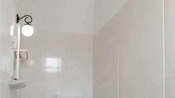 Un baño con inodoro, lavamanos y una lámpara en la pared.