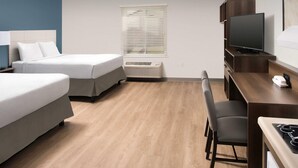 A hotel room with two beds, a desk with a chair, a television, and a window with blinds. - Woodspring Suites Southington (Southington)