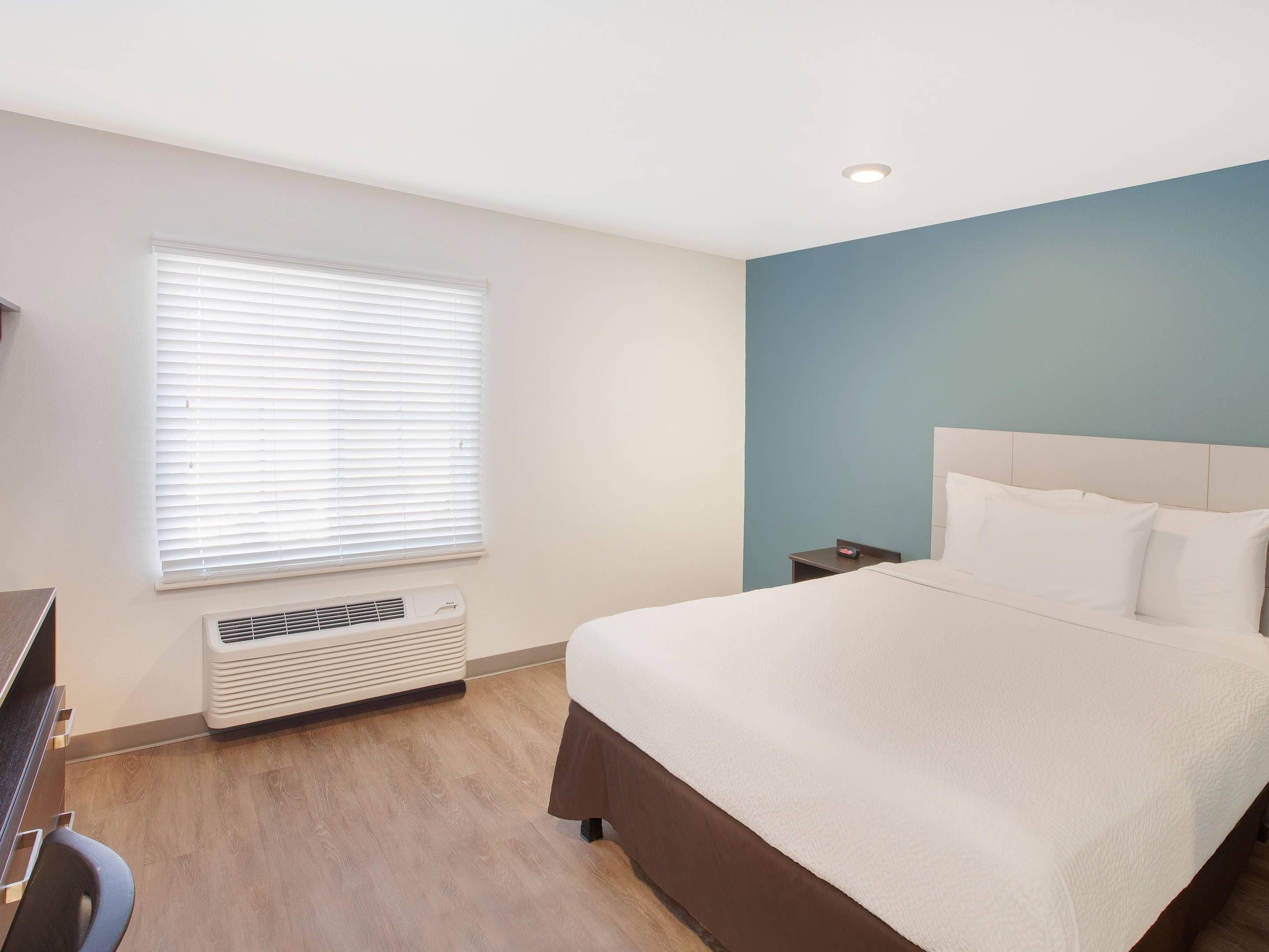 Una habitación de hotel con cama, mesita de noche y ventana con persianas.