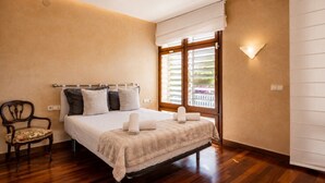 Ein Schlafzimmer mit einem Bett, einem Sessel, einem Fenster mit Jalousien und einer Wandleuchte.
