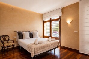 A bedroom with a bed, a chair, a window with blinds, and a wall-mounted light. - Villa Bella - Exclusive Roses Retreat (Girona)