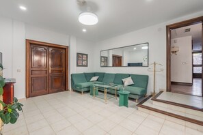 A living room with a green sofa, a glass coffee table, and a wooden door. - Villa Bella - Exclusive Roses Retreat (Girona)