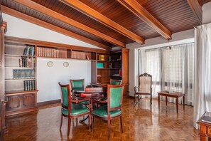 A room with wooden bookshelves, a round table, and green upholstered chairs. - Villa Bella - Exclusive Roses Retreat (Girona)