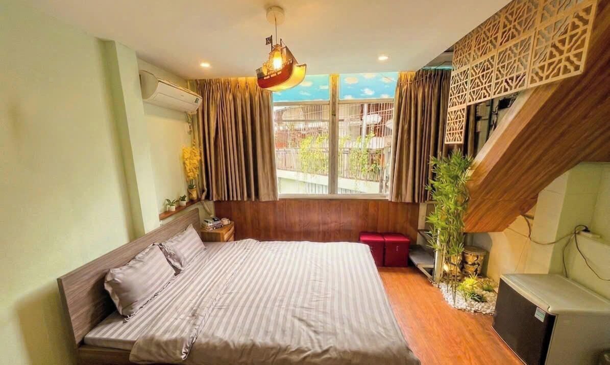 A bedroom with a bed, a desk, a chair, a window with curtains, and a staircase.