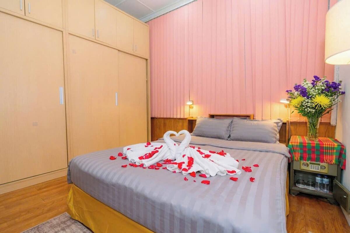 A hotel room with a bed, a wardrobe, a bedside table with a lamp, and a vase with flowers.