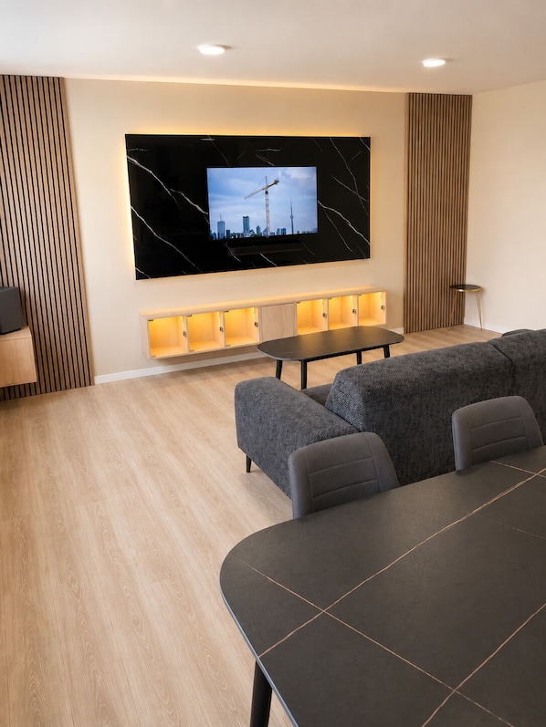 Un salon moderne avec un grand téléviseur, un canapé, une table à manger et un mur d’accent en bois.