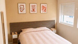 Un dormitorio con cama, mesita de noche y ventana con persianas.