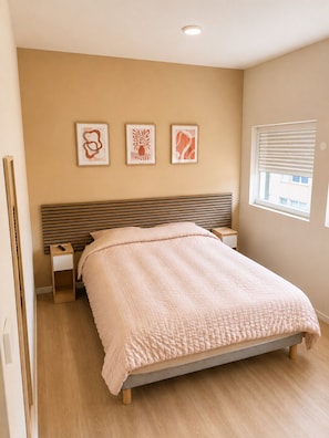 Une chambre à coucher avec un lit, une table de chevet, une commode et une fenêtre avec des stores.