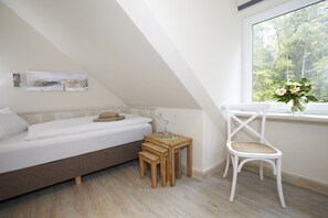 A bedroom with a loft bed, a small wooden table, a white chair, and a window with a view of trees. - Apartment fur 8 Personen mit Balkon in Uckeritz (Ueckeritz)