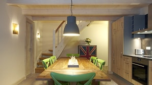 Uma área de refeições com mesa de madeira, cadeiras verdes, luminária pendente, escada e uma cozinha com armários e eletrodomésticos.