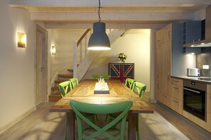 A dining area with a wooden table, green chairs, a pendant light, a staircase, and a kitchen area with cabinets and appliances. - Apartment fur 8 Personen mit Balkon in Uckeritz (Ueckeritz)