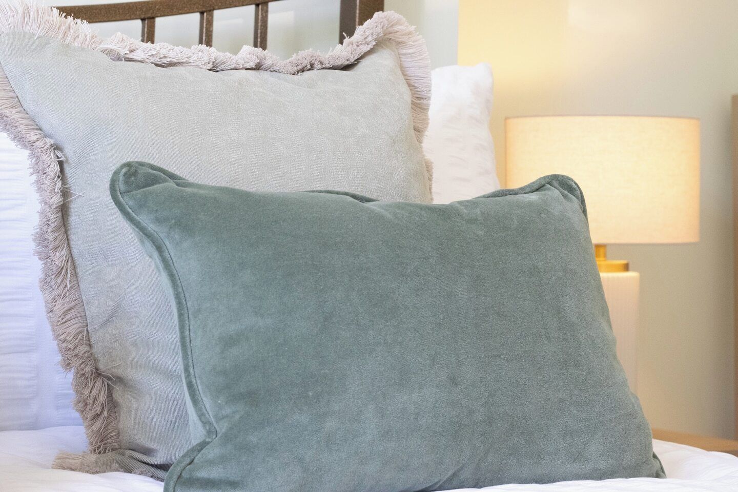Un lit avec deux oreillers, un blanc et un vert, et une lampe de chevet.