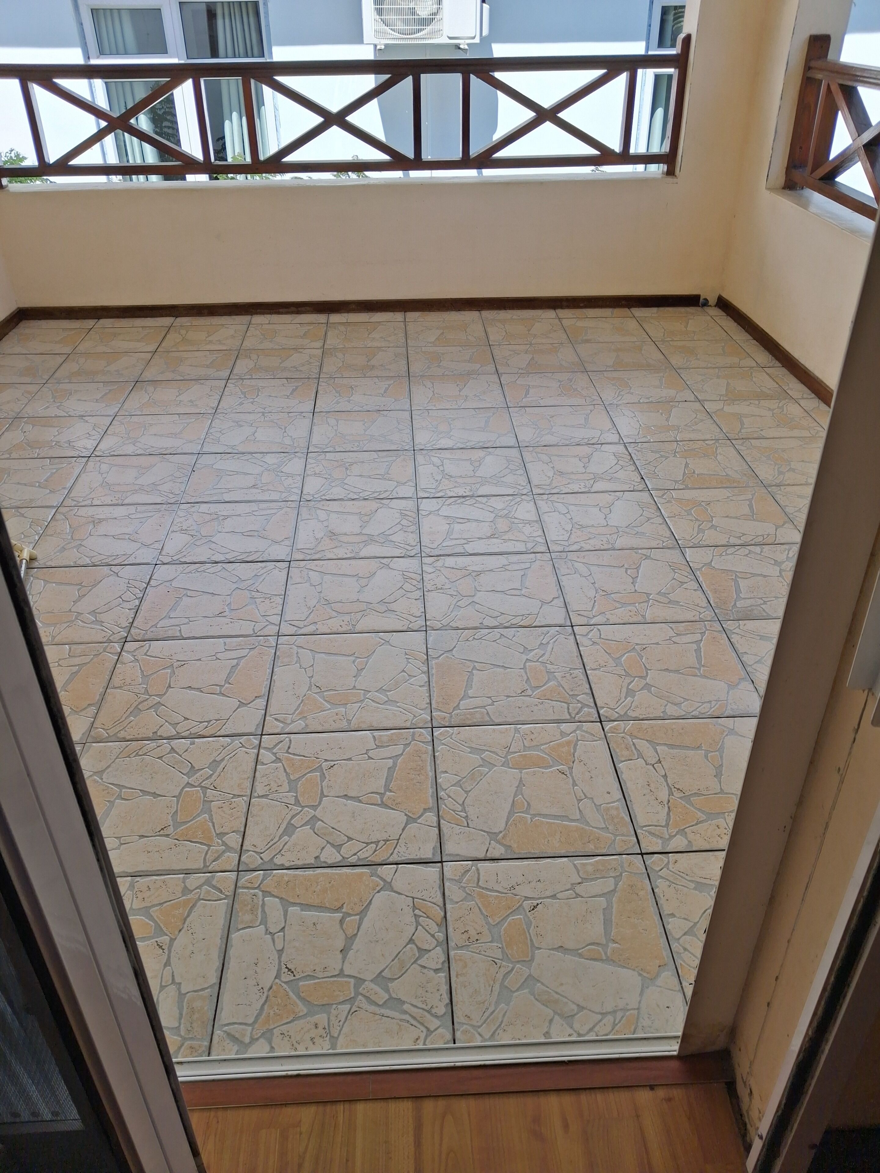 Ein Zimmer mit Fliesenboden, einem Holzboden im unteren Bereich und einem Balkon mit Geländer.