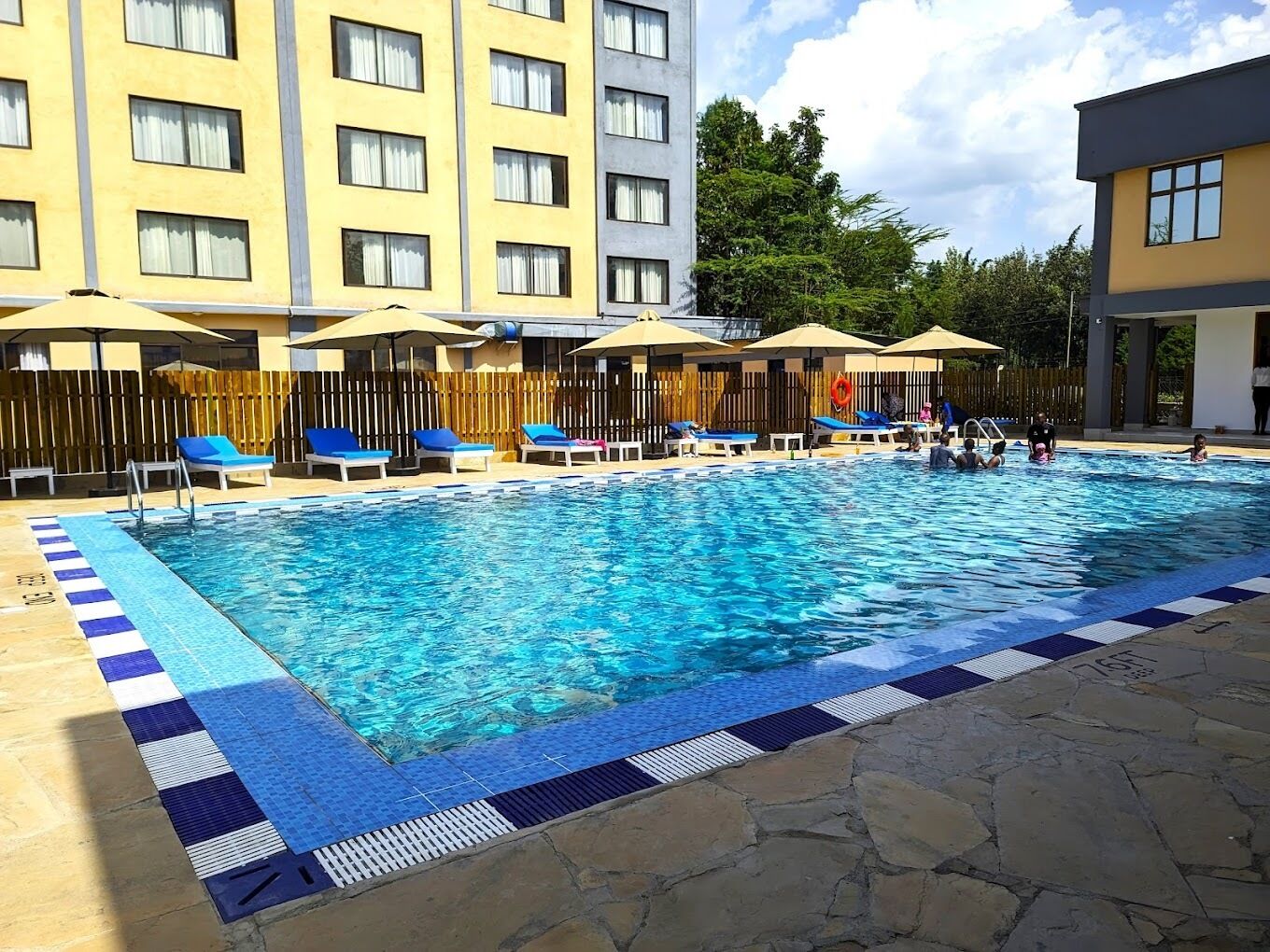 A swimming pool with lounge chairs and umbrellas, surrounded by a hotel building.