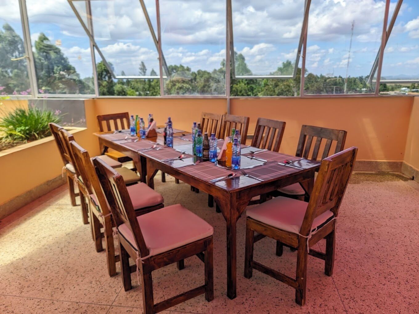 Una mesa redonda de madera con sillas, botellas de agua y vistas a árboles a través de una ventana.