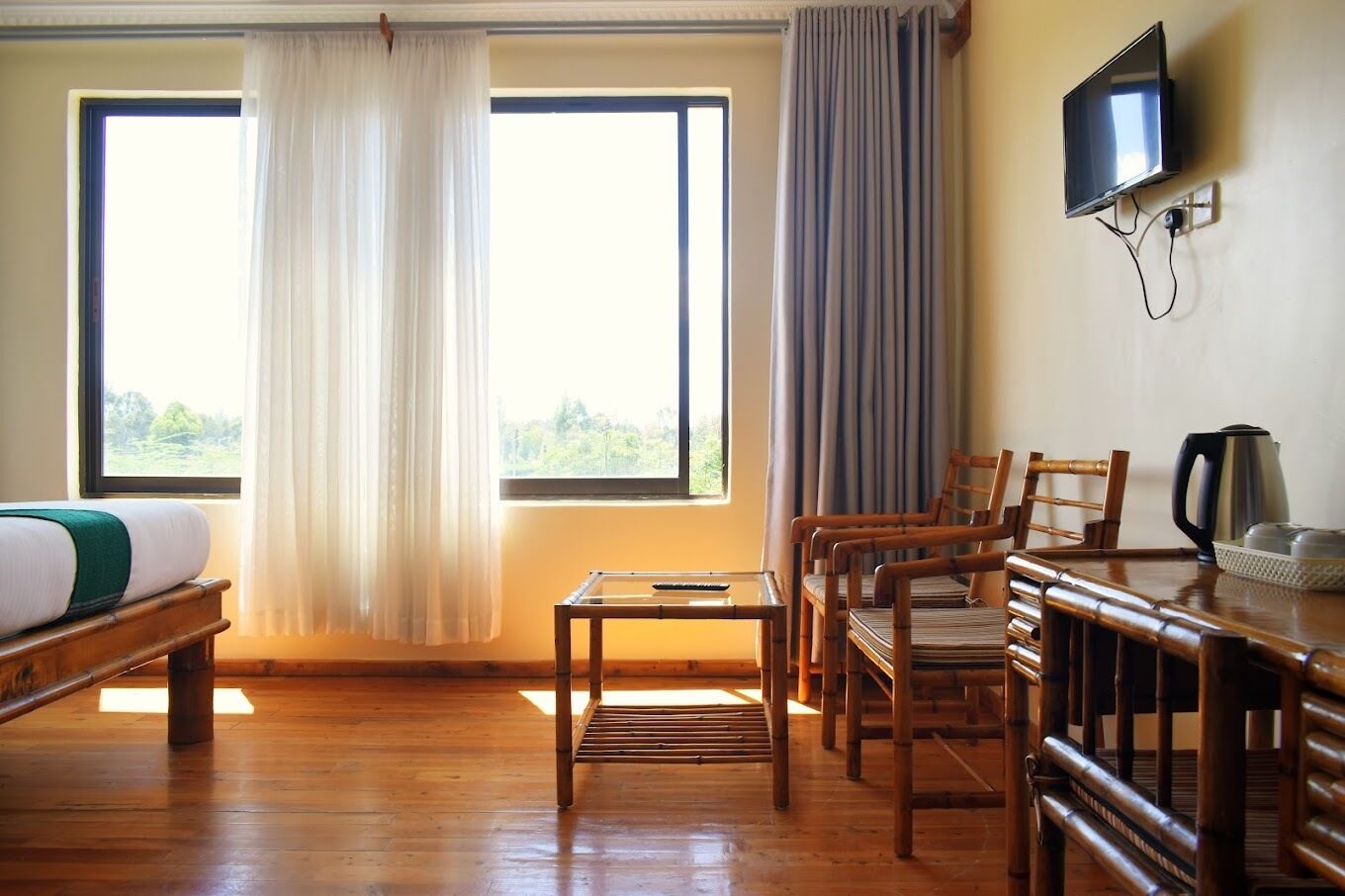A room with a bed, a table, chairs, a TV, and a window with curtains.