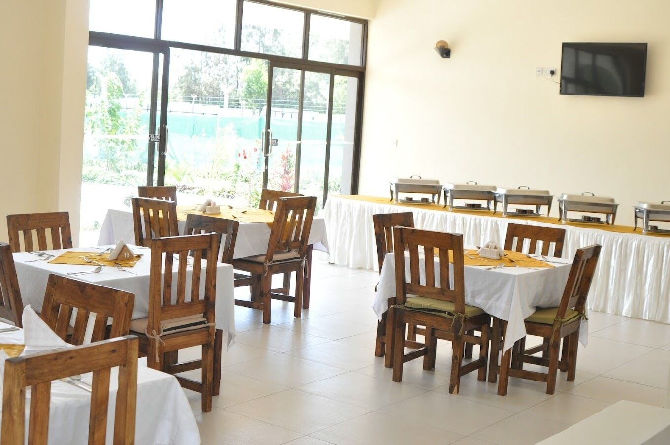Un'area pranzo con tavoli e sedie, un'ampia finestra e un televisore a parete.