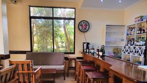 Una zona de bar con mobiliario de madera, un ventanal con vistas a árboles y un letrero en la pared.