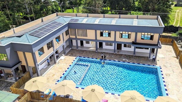 Un edificio de varios pisos con piscina, paneles solares en el techo y un área exterior cercada.