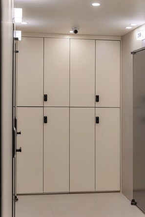 A hotel room with a large wardrobe, a door with a security camera, and a number sign on the wall.