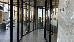 A modern interior with glass doors leading to a gym area, a marble wall, and a sign indicating a kitchenette. - The Rich Rama 9 - Srinakarin (Khet Suan Luang)