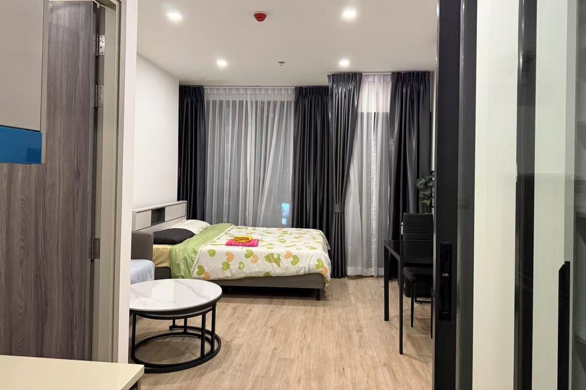 A modern hotel room with a bed, a small round table, a desk, and a chair.
