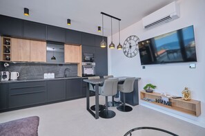 Eine moderne Küche mit eingebauten Geräten, eine Essecke mit Tisch und Stühlen und ein großer Flachbildfernseher an der Wand.