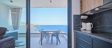 Cocina moderna con encimera de mármol negro, cafetera y vista al mar a través de un ventanal corredera.