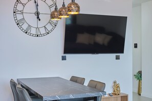 Ein moderner Essbereich mit einem Marmortisch, Ledersesseln, einem großen Flachbildfernseher und einer dekorativen Wanduhr.