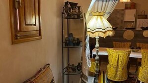 A cozy room with a wooden door, a shelf with decorative items, a table with a yellow tablecloth, and a hanging lamp.