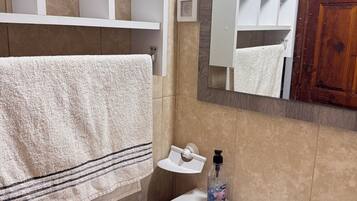 A bathroom with a white sink, a mirror, a towel hanging on the wall, and a shelf above the sink.