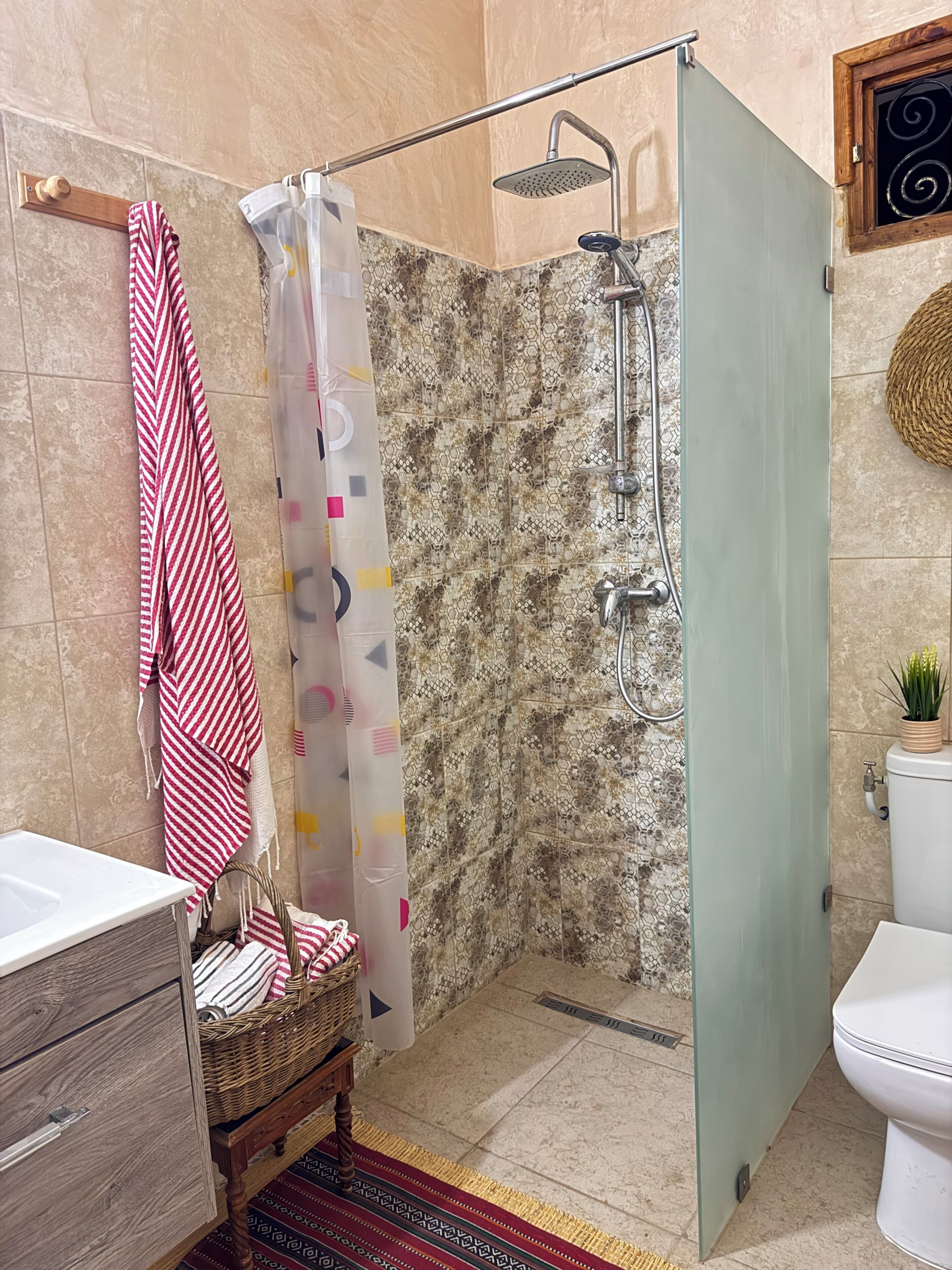 A bathroom with a shower, a toilet, a sink, a towel rack, and a wicker basket.