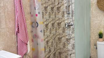 A bathroom with a shower, a toilet, a sink, a towel rack, and a wicker basket.
