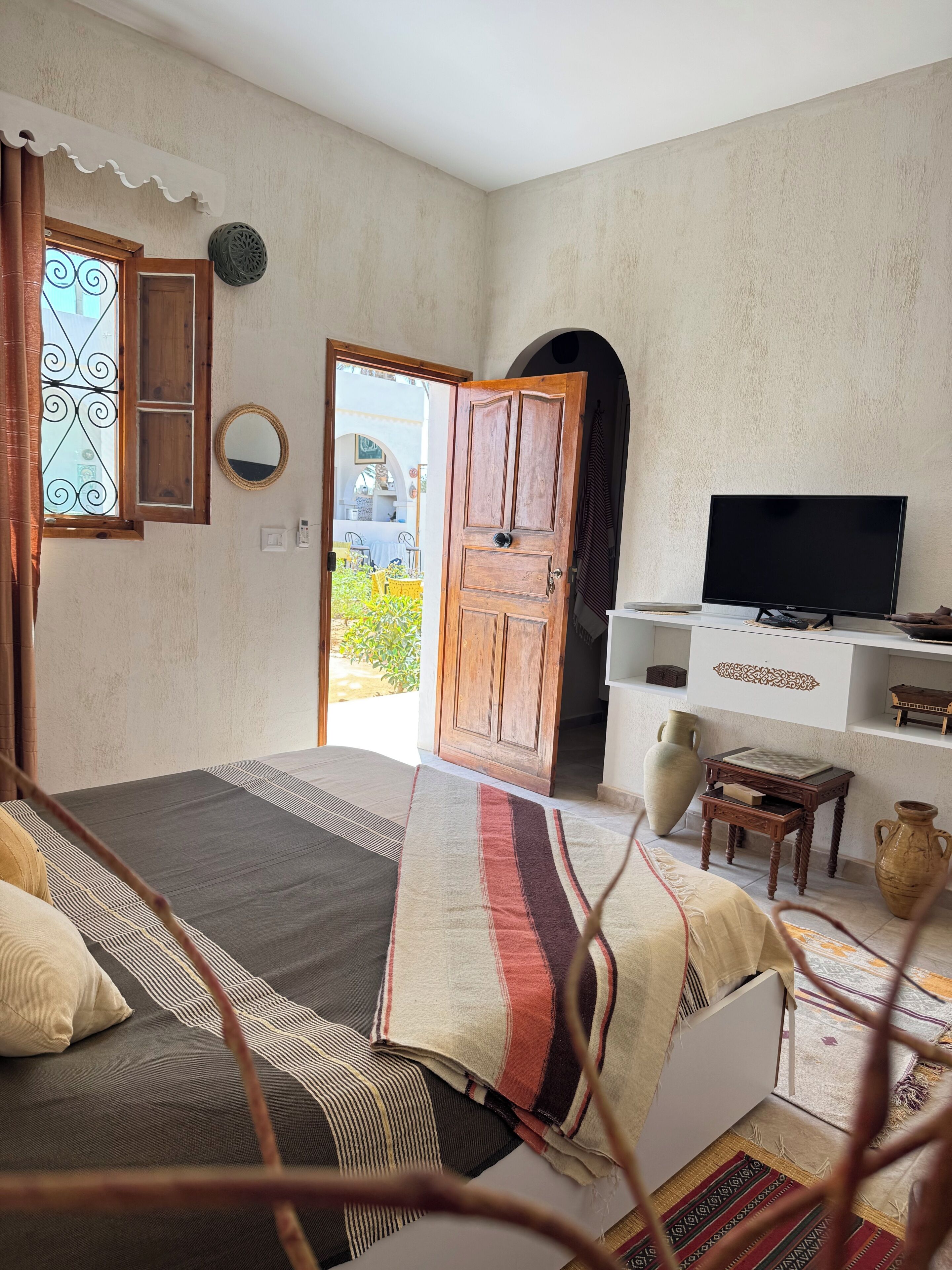 Un dormitorio con cama, televisión, puerta de madera y vistas al exterior.