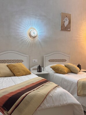 A hotel room with two beds, a nightstand, a wall-mounted light fixture, and a framed picture. - Djerba rêve vacances Suite Noura (El May)