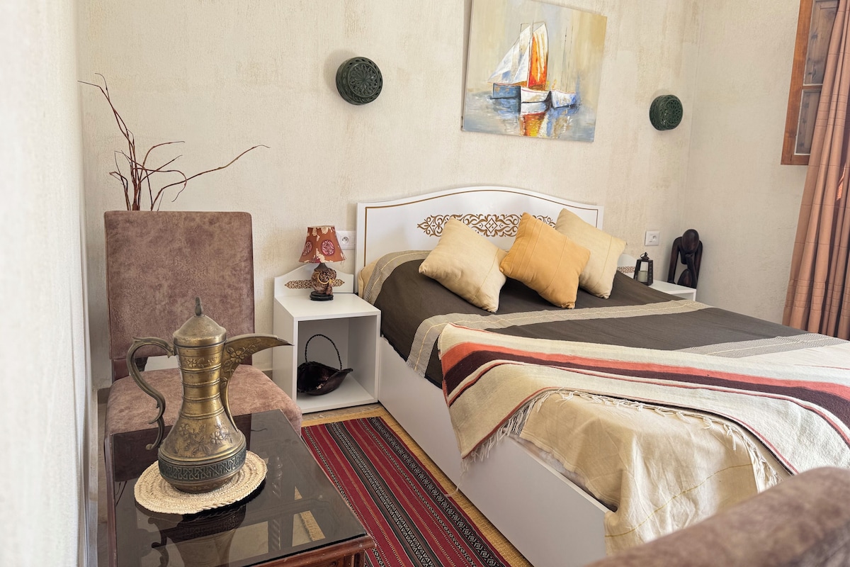 Une chambre à coucher comprenant un lit, des tables de chevet, une lampe, un vase décoratif, un tableau et un tapis.