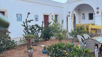 A courtyard with a dining area, potted plants, and a white building with arches.