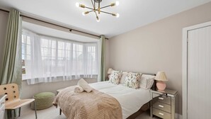 A bedroom with a bed, bedside tables, a chair, a window with curtains, and a ceiling light fixture. - Spacious Modern home in Whitefield - Sleeps 9 (Whitefield)