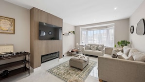 A modern living room with a flat-screen TV, a fireplace, a sofa, and a coffee table. - Spacious Modern home in Whitefield - Sleeps 9 (Whitefield)