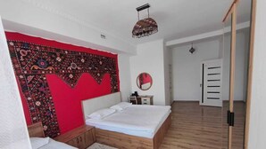 Un dormitorio con dos camas, un tapiz rojo, piso de madera, un espejo y un armario.