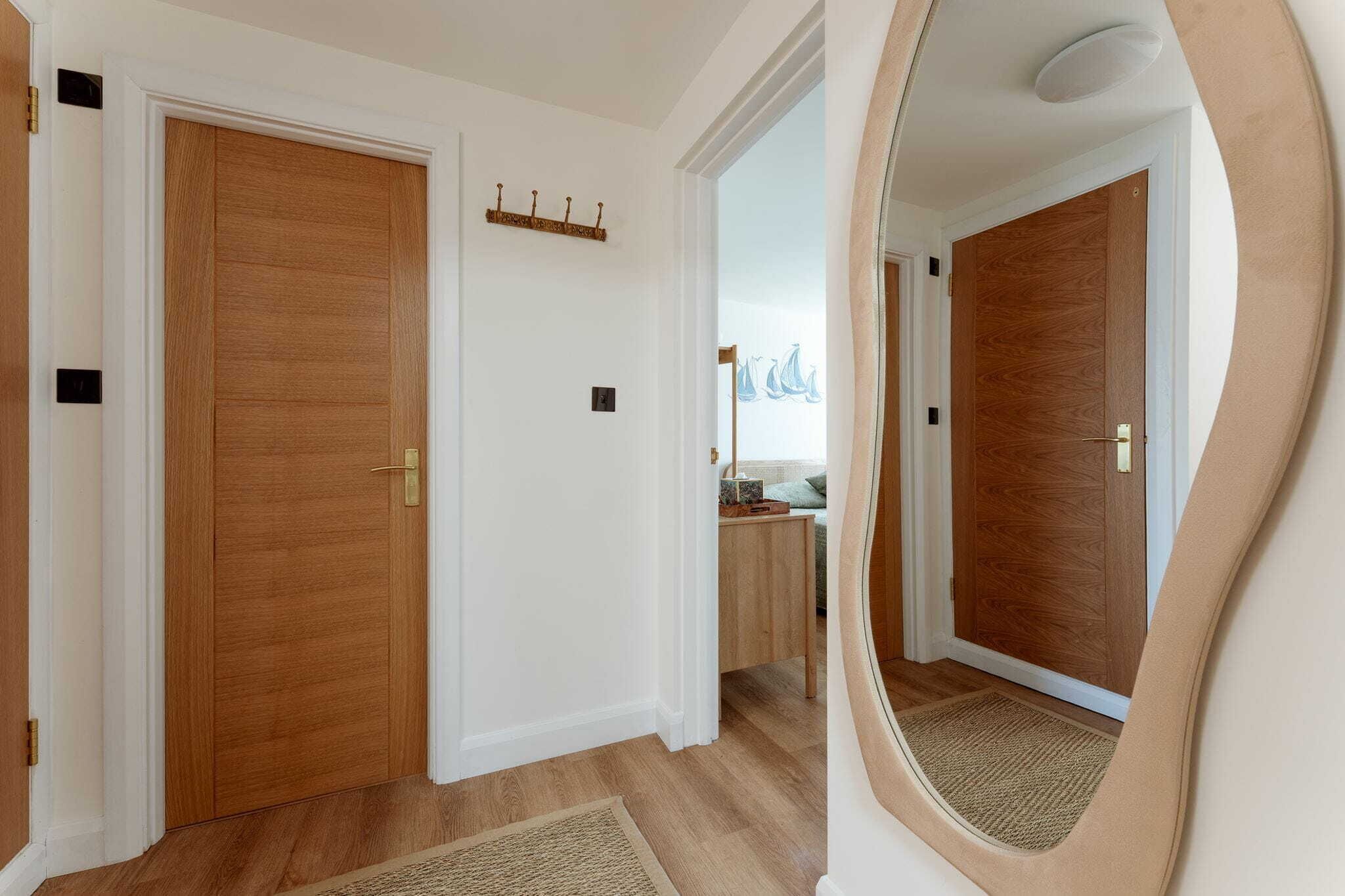 A hallway with wooden doors, a coat rack, and a small table with a lamp.