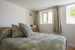 Un dormitorio con cama, almohadas, mesita de noche, lámpara y ventana con cortinas.