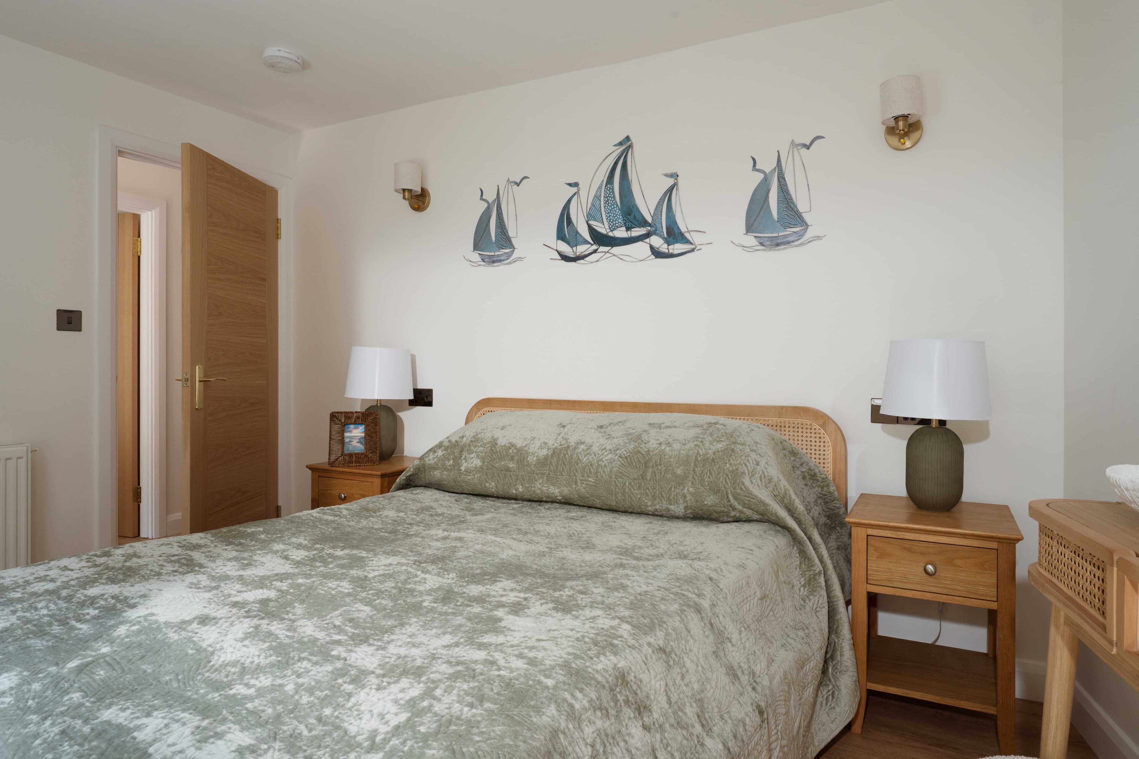 A bedroom with a bed, two bedside tables with lamps, a wooden door, and wall art of sailboats.