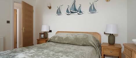 A bedroom with a bed, two bedside tables with lamps, a wooden door, and wall art of sailboats.