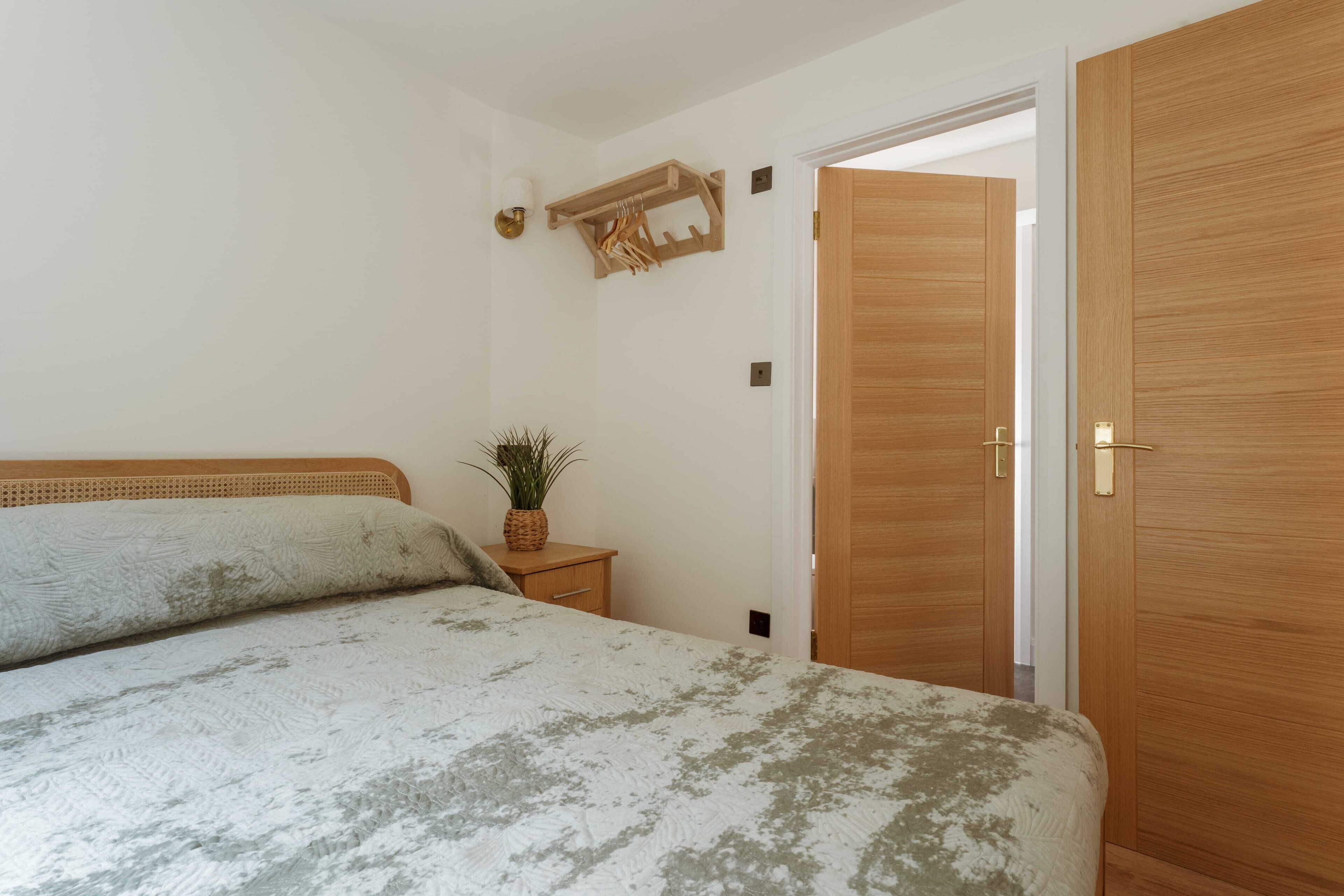 Een slaapkamer met een bed, een houten garderobe, nachtkastje met een plant en een wandlamp.
